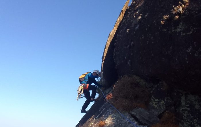 Pessoa escalando parede de Rocha com céu e mar ao fundo do